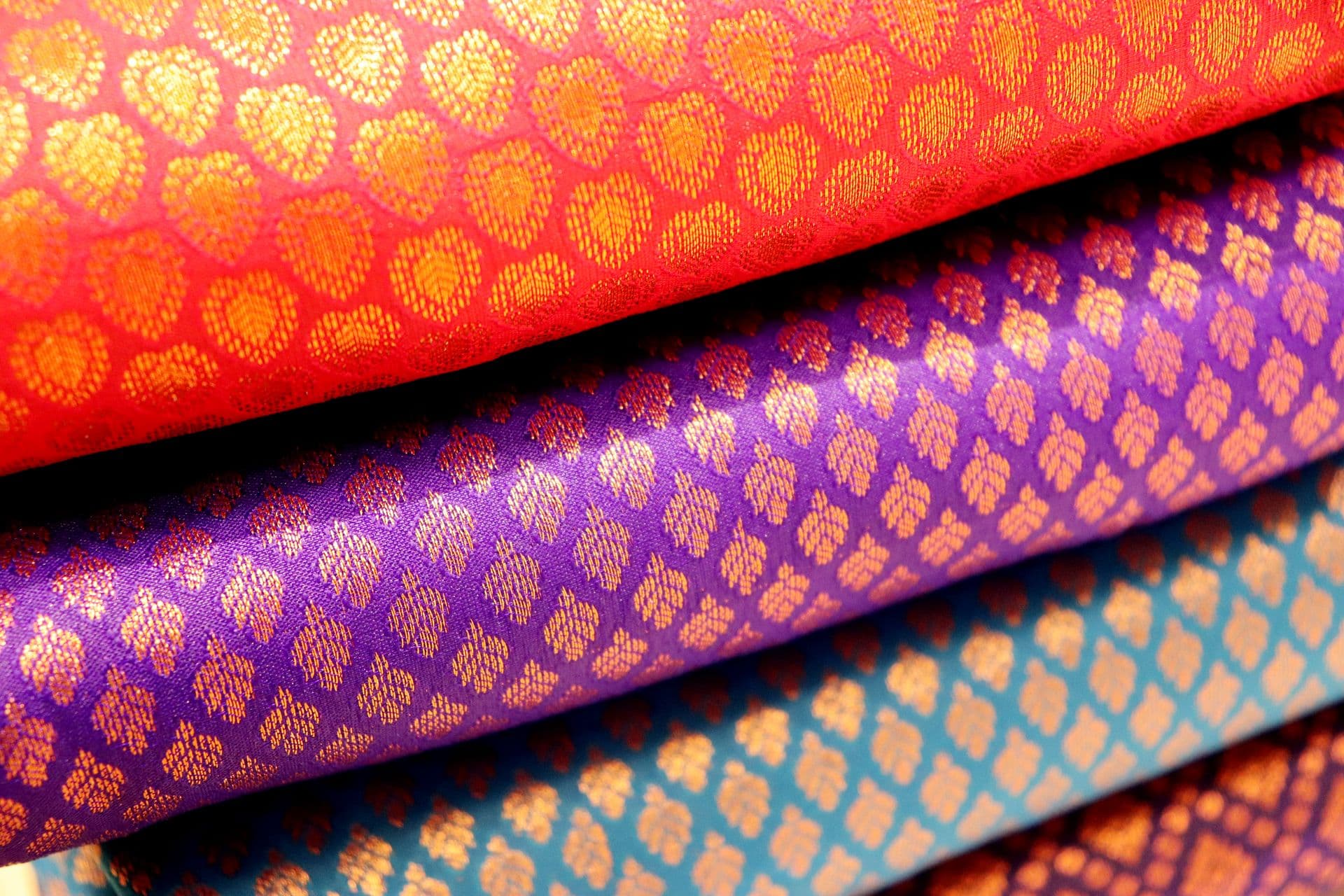 Folded Kanchipuram silks in red, purple and teal, woven all over with small gold motifs